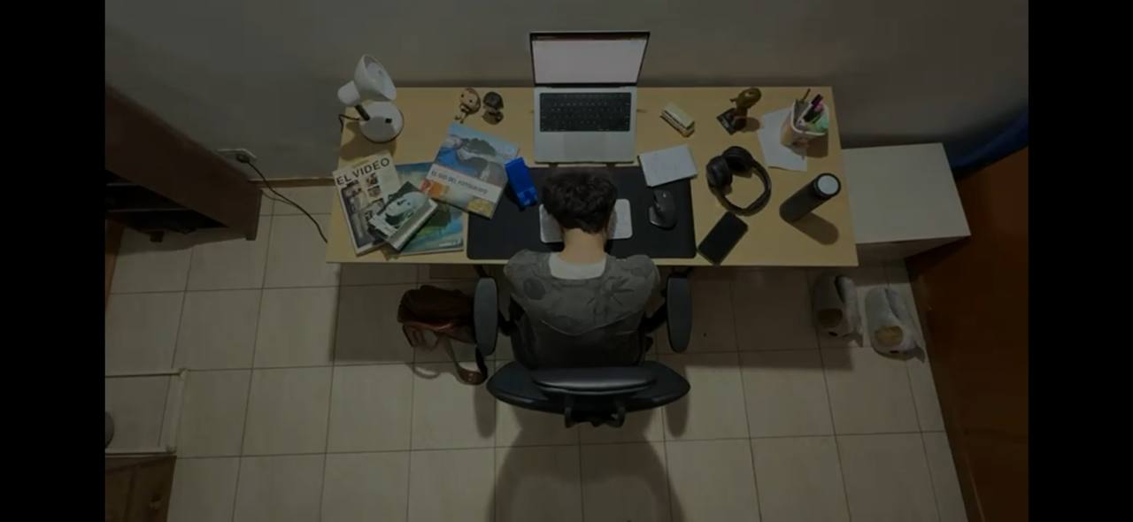 Top view of a person sitting at a desk with a laptop, headphones, books, lamp, and stationery organized around.
